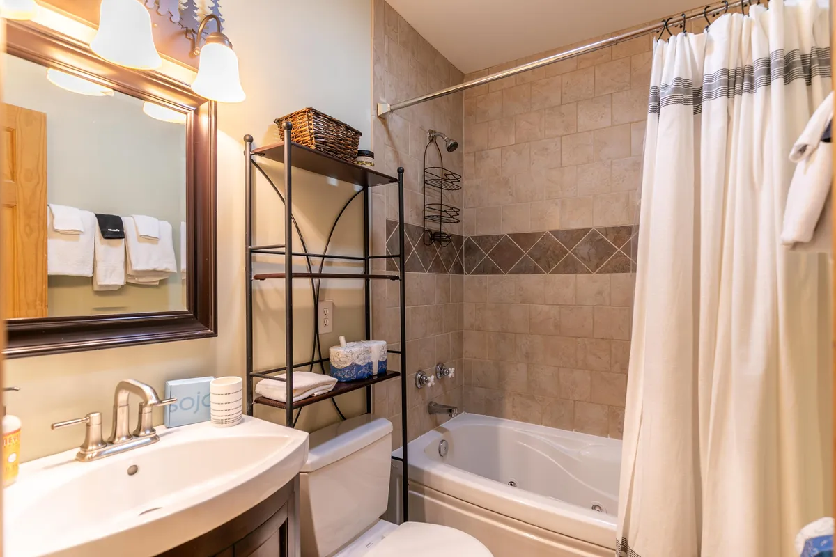 A bright, spa-like bathroom with a large bathtub, elegant sink, mirror, and towel rack. The space is designed for relaxation, offering a soothing spot to unwind after a day of adventure.
