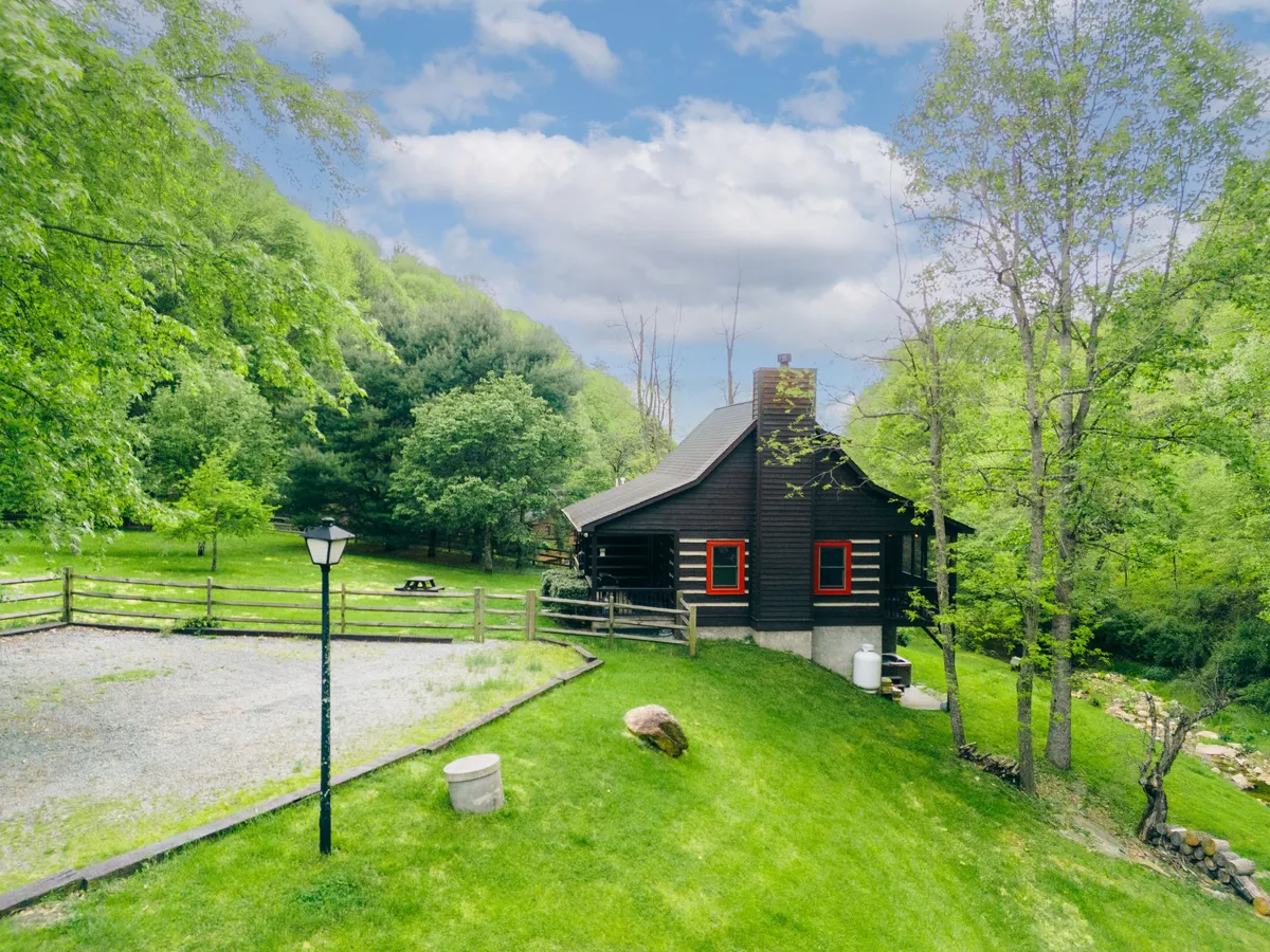 This image captures the log cabin set against a lush green landscape, featuring a spacious, fenced area and a classic lamp post. The fenced yard is clearly visible, offering a sense of safety and ample space for children to play and families to gather and explore the outdoors.