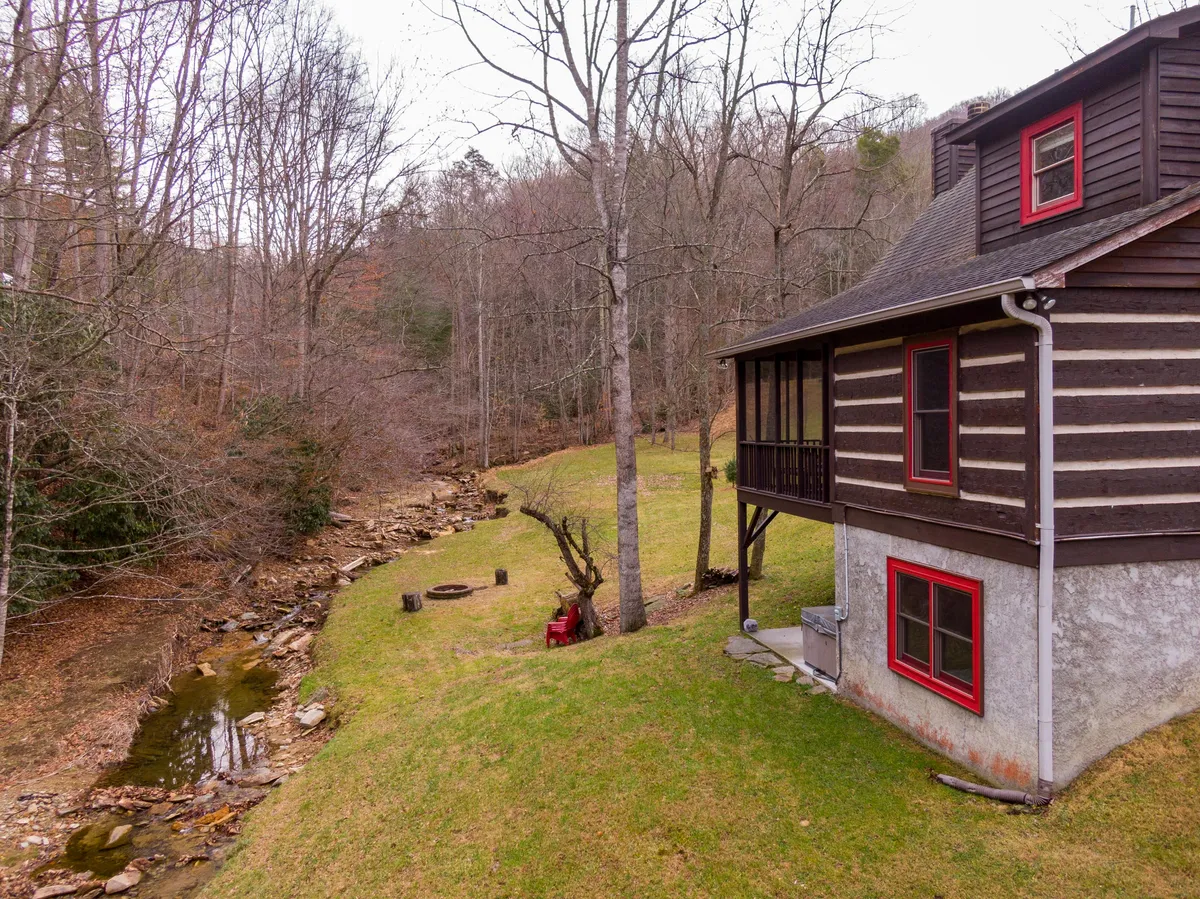 A rustic wooden cabin nestled beside a tranquil stream, with a cozy fire pit surrounded by natural forest and trees. The scene captures the serenity of the outdoors, including the gentle flow of the creek, inviting nature walks, and a peaceful retreat atmosphere.