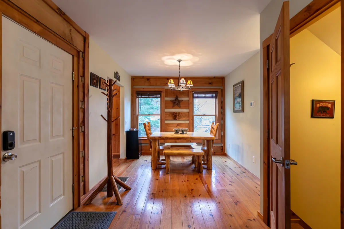 A sunlit dining area with a striking wooden Aspen table, rustic chairs, and a statement chandelier. Windows open up to mountain views, enhancing the sense of place and warmth. The setting is perfect for family meals and shared laughter.