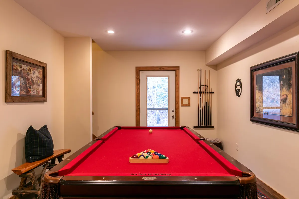 A vibrant game room featuring a pool table, wooden accents, framed artwork, and pool cues neatly arranged. The space is inviting and designed for friendly gatherings and relaxed entertainment.