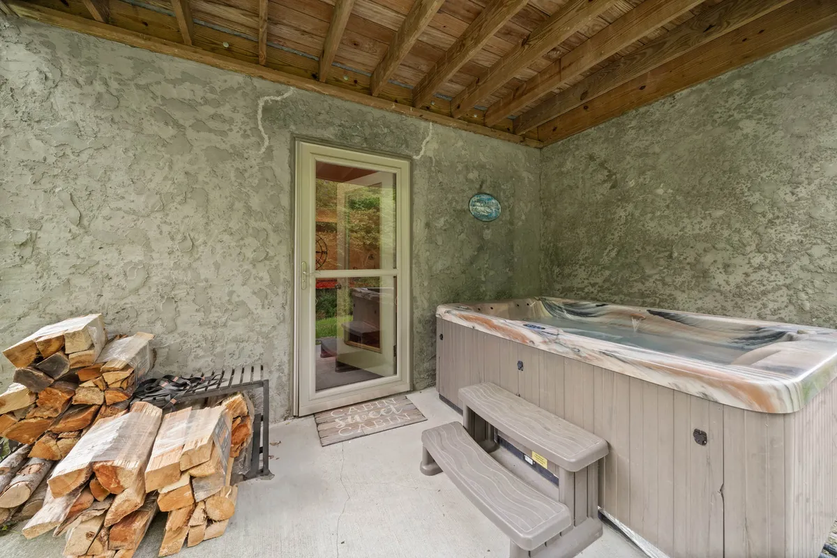 Inside the screened porch, a bubbling hot tub sits beside a stack of wood and a doorway leading outside. The tranquil setting invites relaxation and family connection, with an easy transition between indoor and outdoor fun.